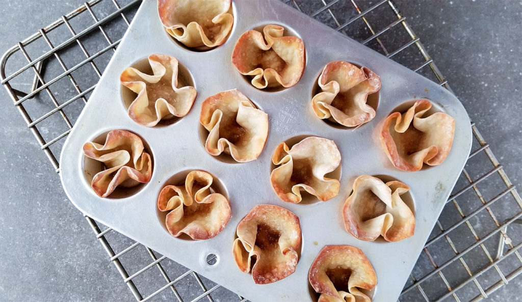 baked wonton wrappers in a muffin tin on a cooling rack