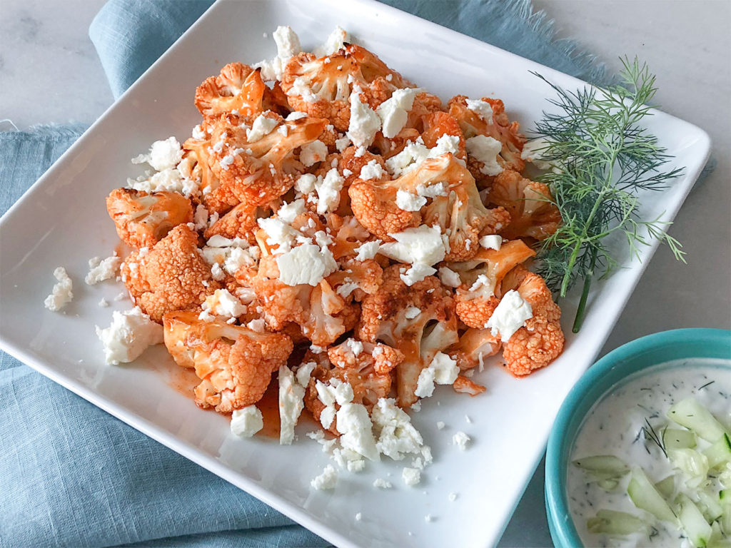 Buffalo Cauliflower on a plate topped with feta cheese with a side of tzatziki sauce