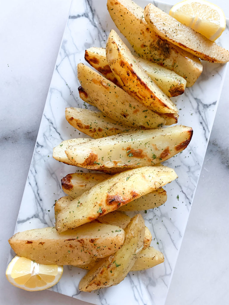 Greek lemon potatoes arranged on a plate with lemon wedges