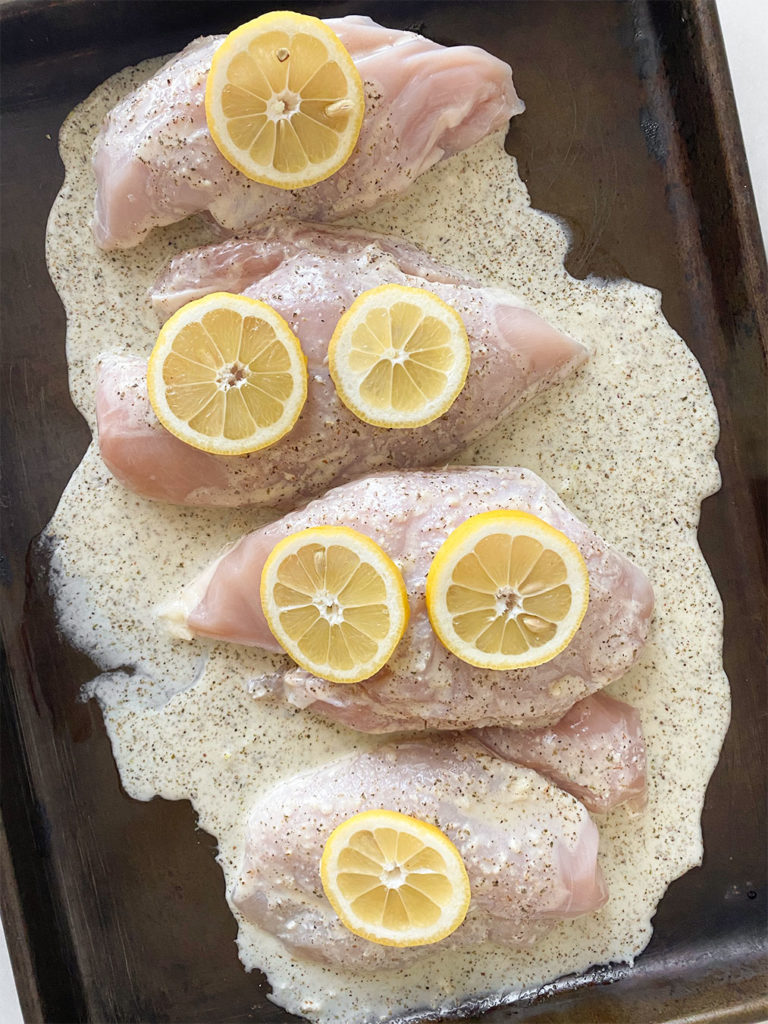 Uncooked chicken breasts topped with lemon sauce and lemon slices