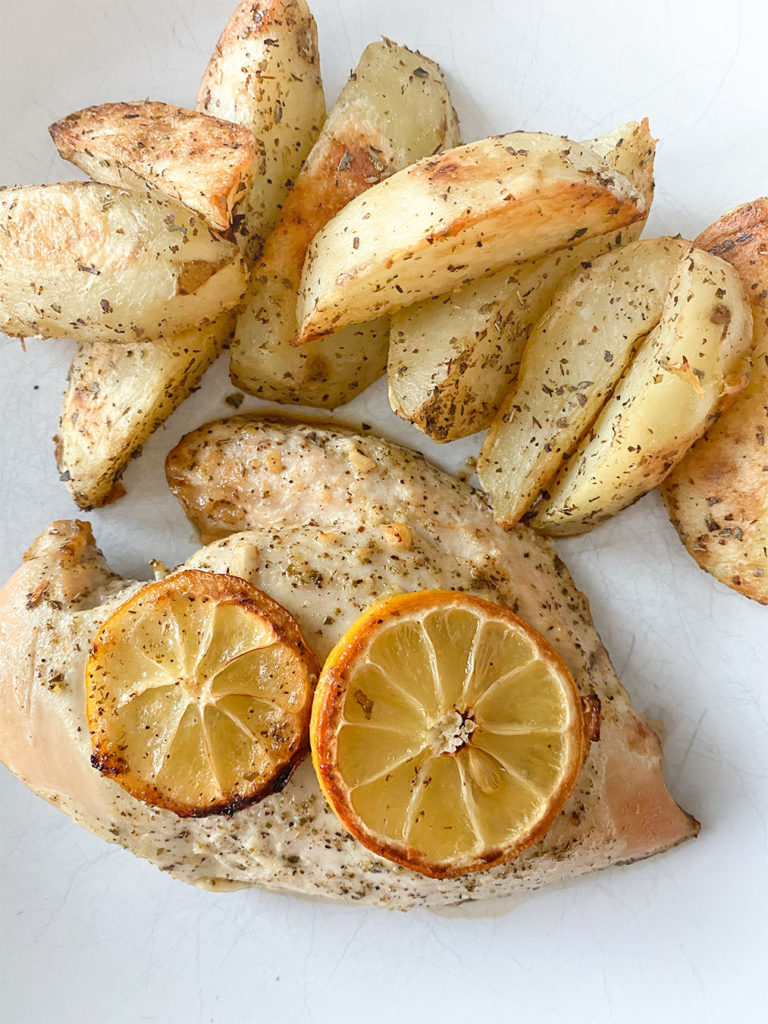 Cooked lemon chicken breasts on a plate served with greek lemon potatoes