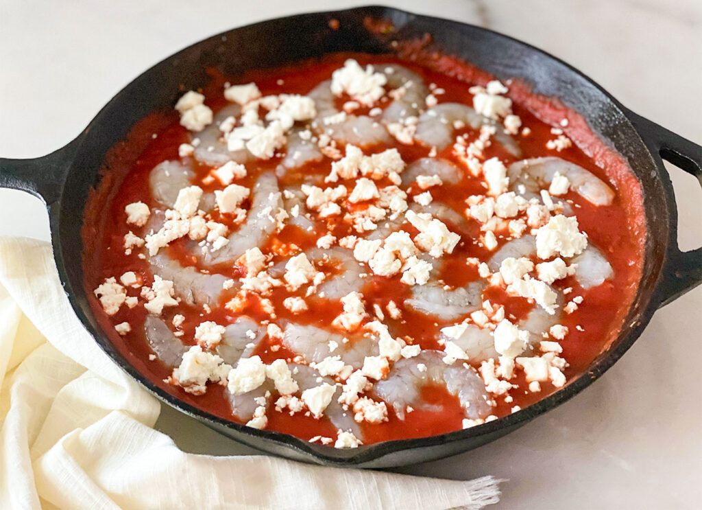 Tomato sauce, raw shrimp and feta cheese in a cast iron skillet